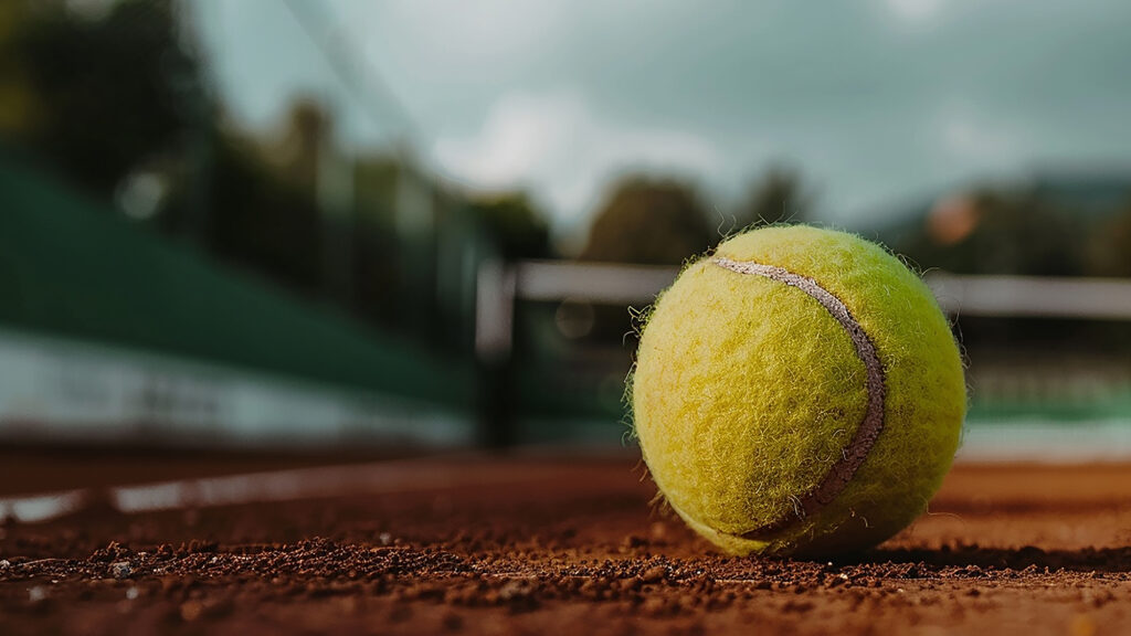 pelota de tenis en primer plano con el fondo de una cancha de tenis desenfocada